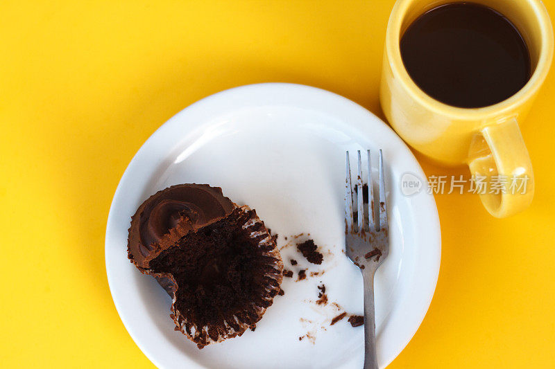 Yum !白色盘子上的巧克力杯蛋糕(吃了一半)，明亮的黄色背景